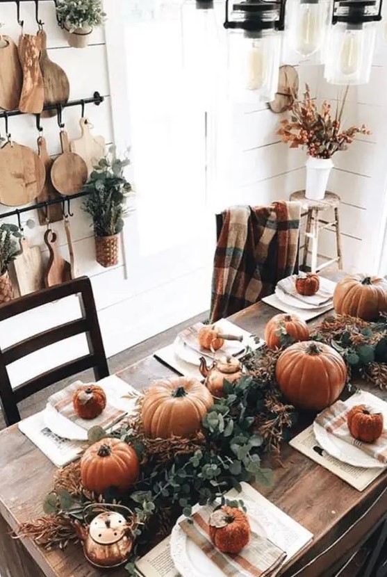 a simple rustic Thanksgiving table with a lush greenery runner, rust pumpkins and gourds, copper teapots and mugs