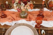 35 a warm-colored boho Thanksgiving tablescape with a white and orange table runner, a dried flower and pampas grass bouquet, a woven placemat and rust napkins