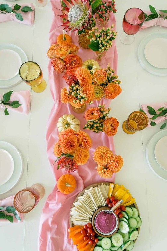 a pink and orange Thanksgiving table setting with a pink runner and orange blooms, orange and pink glasses and pink napkins