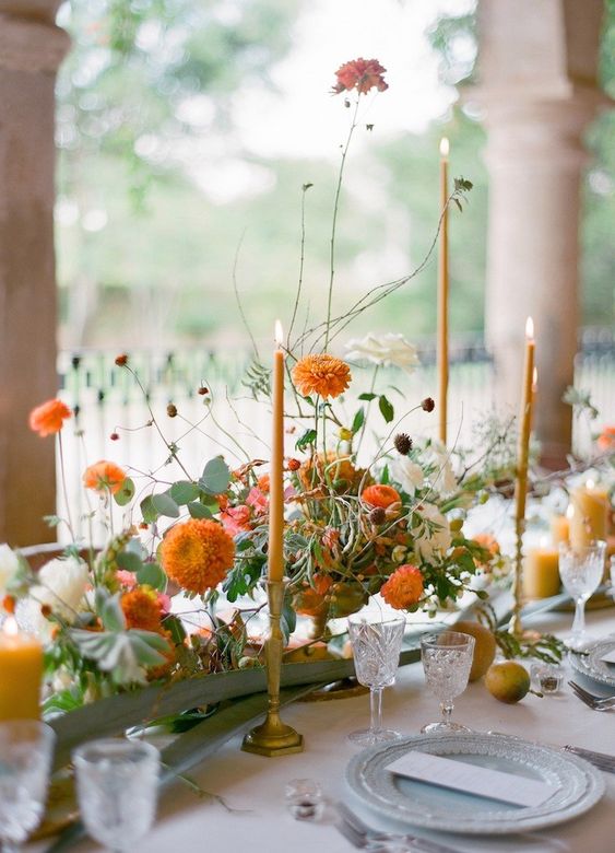 a sophisticated Thanksgiving tablescape with orange blooms and candles, with blue porcelain and orange candles