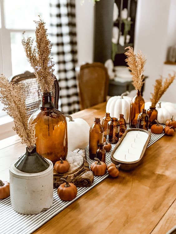 boho meets rustic Thanksgiving decor with dark bottles with grasses, mini faux pumpkins and large white ones, a large candle
