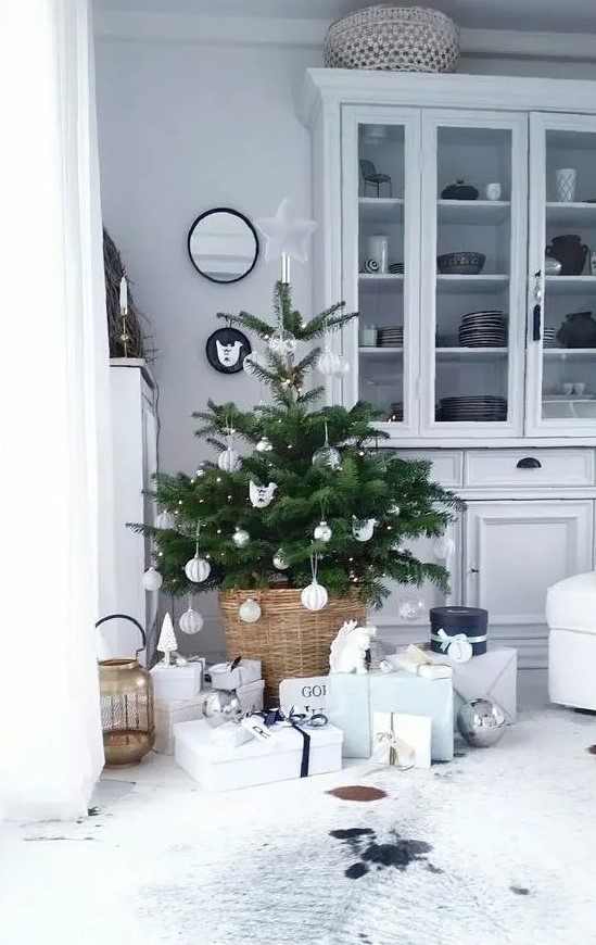 a small Nordic Christmas tree with lights and white and silver ornaments placed in a basjet and with neutral gift boxes under it is a chic idea for a modern space
