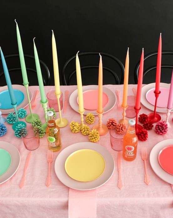 a rainbow Thanksgiving tablescape with bright plates and candles, bold pinecones and pink cutlery is very unusual