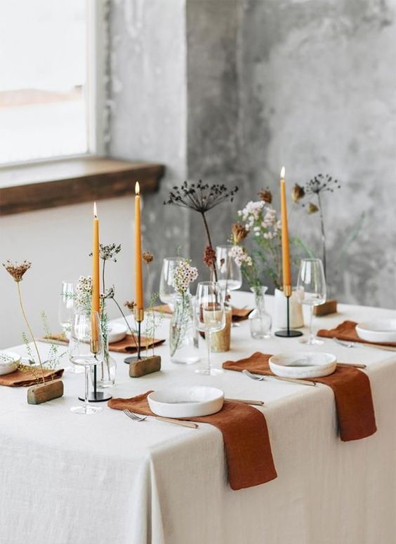 a stylish modern meets boho Thanksgiving tablescape with rust napkins and candles, fresh and dried blooms, white plates and wooden stands