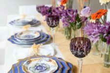 40 a stylish Thanksgiving table setting with a neutral runner, purple and orange blooms, wheat, blue plates with a gold edge, gold cutlery