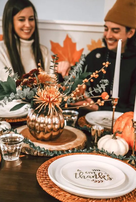 orange woven placemats, orange blooms and berries and orange pumpkins add color and coziness to the Thanksgiving tablescape