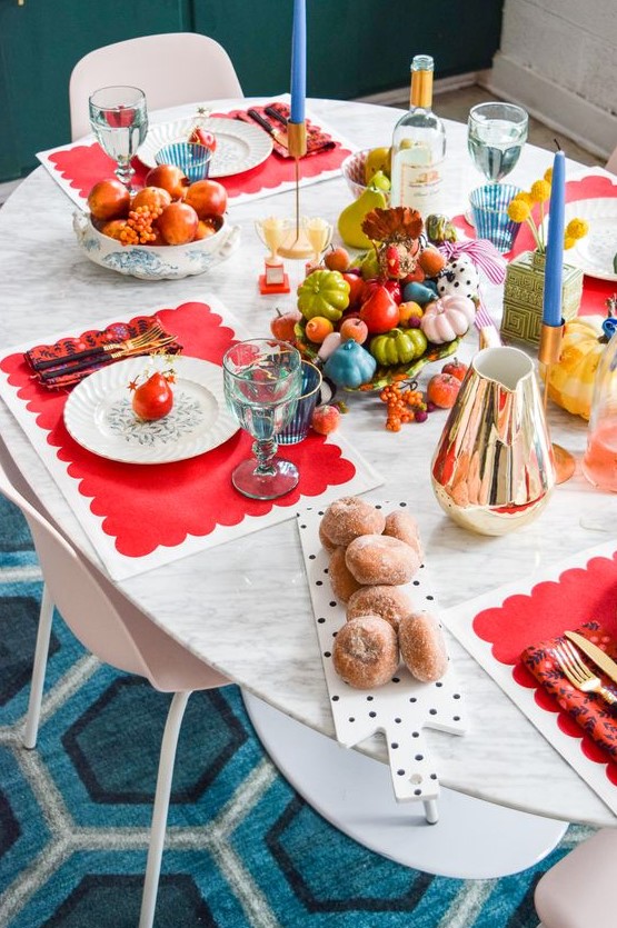 a super colorful Thanksgiving table setting with red placemats, blue candles, colorful faux veggies and blue glasses