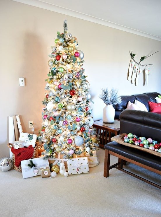 a flocked Christmas tree decorated vintage style with silver, pink, red and light green ornaments, fresh greenery and lights looks magical