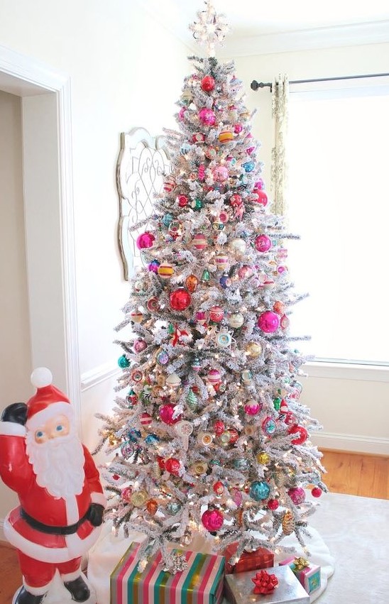 a flocked Christmas tree decorated with red, pink, green, yellow and silver ornaments of various sizes and shapes and spruced up with lights