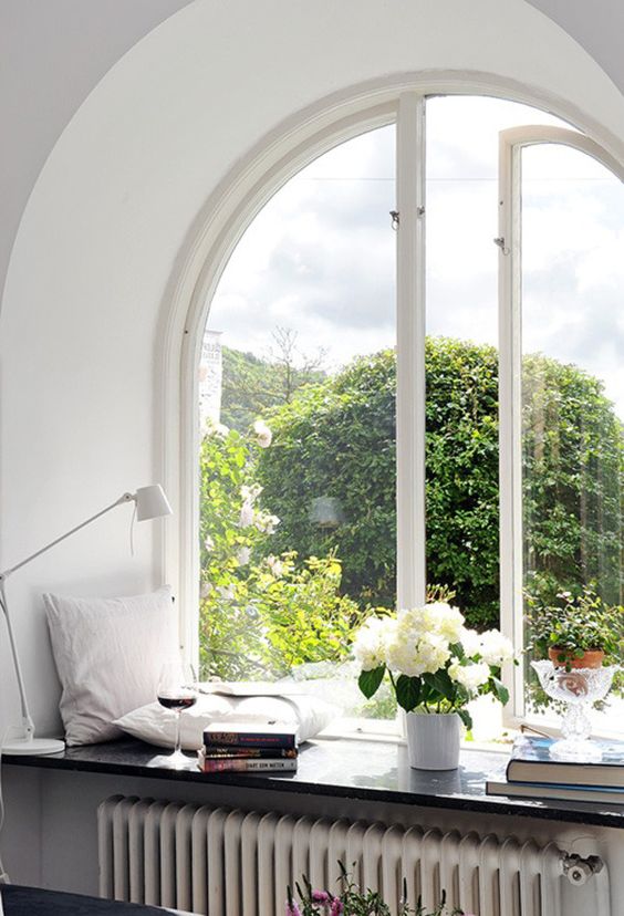 a beautiful arched casement window, a windowsill styled with pillows, blooms and greenery and book stacks are very cozy and chic