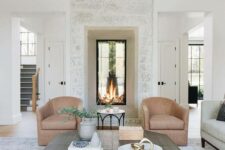 a beautiful neutral living room with a built-in double-sided fireplace, beige chairs, a grey coffee table and wooden beams
