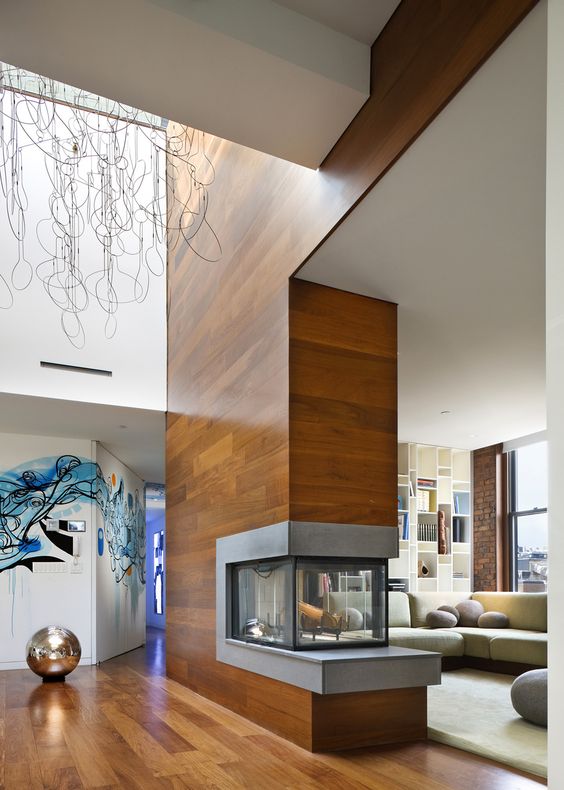 a built in double sided fireplace clad with wood that matches the floor, it separates the entryway and living room