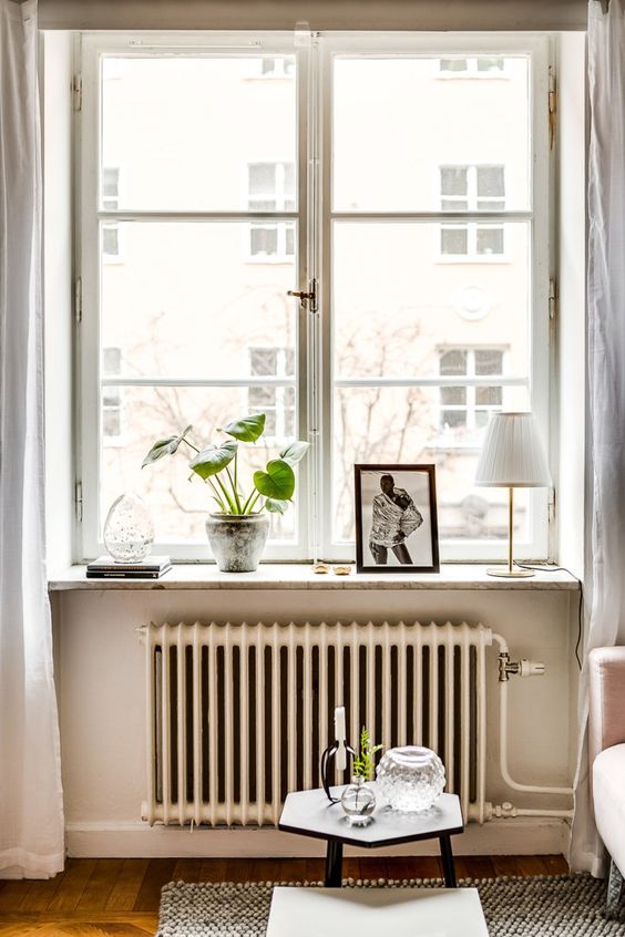 a casement window paired with a vintage radiator and some potted plants and artworks add vintage chic to the space