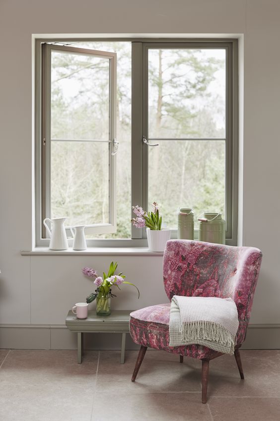 a chic cottage inspired space with a green frame casement window, a green bench and a pink floral chair plus some blooms