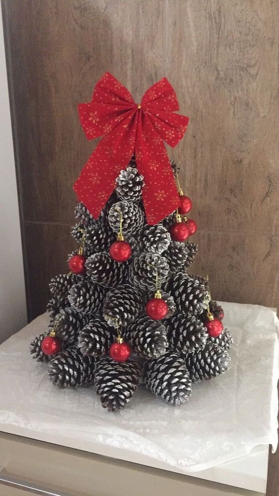 a cone-shaped Christmas tree made of snowy pinecones, decorated with red ornaments and topped with a red bow