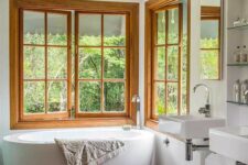a contemporary bathroom with a bathtub placed in the corner by two wood frame casement windows is amazing