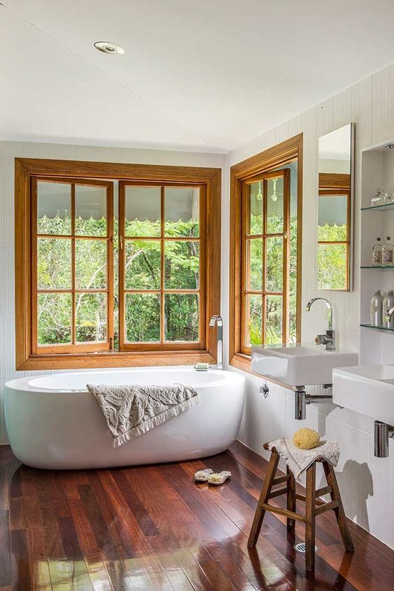 a contemporary bathroom with a bathtub placed in the corner by two wood frame casement windows is amazing