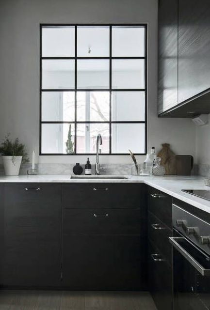 a contemporary black kitchen with white stone countertops and an interior window to the bedroom to provide the kitchen with more light