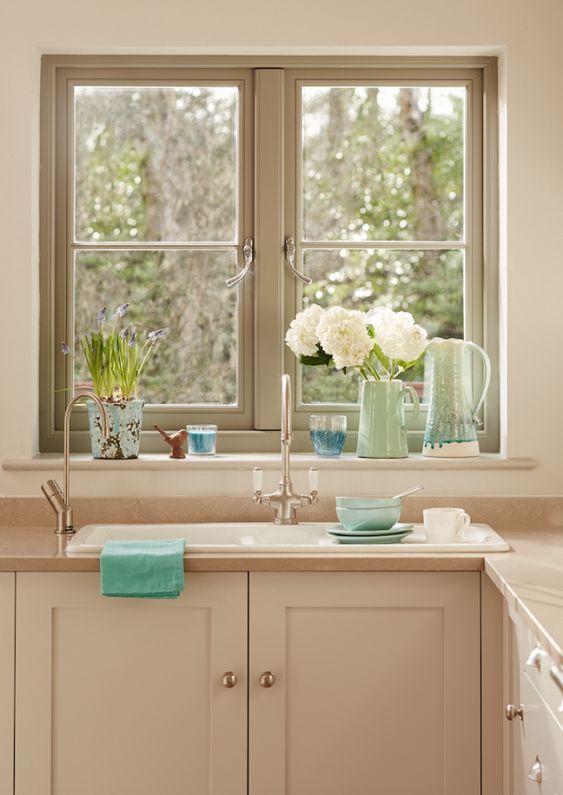a cute modenr cottage kitchen in soft warm neutrals, with a window with green frames, tan cabinets and a beige countertop