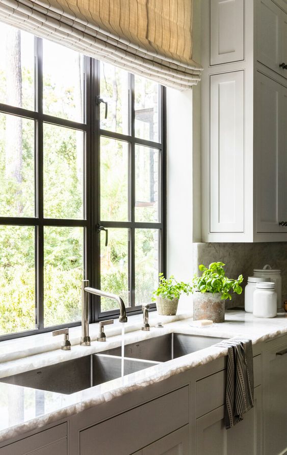 a farmhouse kitchen with shaker style cabinets, a stone countertop, a black frame casement window and striped curtains