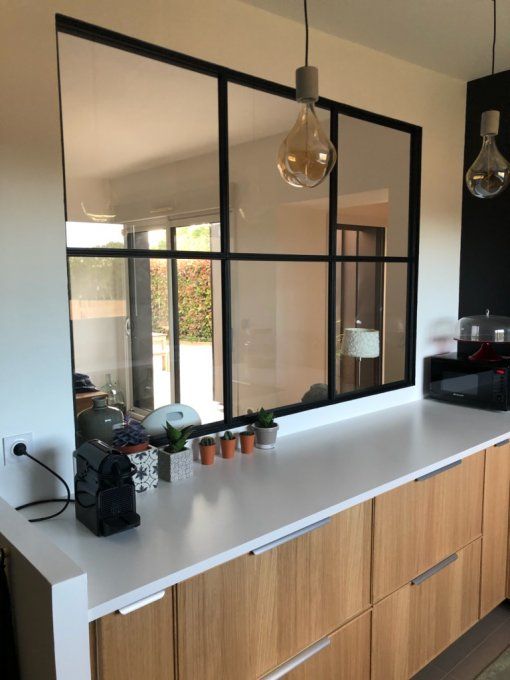 a kitchen and an entryway connected with each other through a window with black frames let fill the entryway with natural light