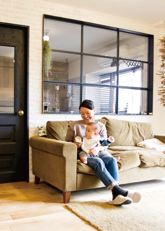 a large window with black framing connects the living room and the kitchen and lets more natural light inside