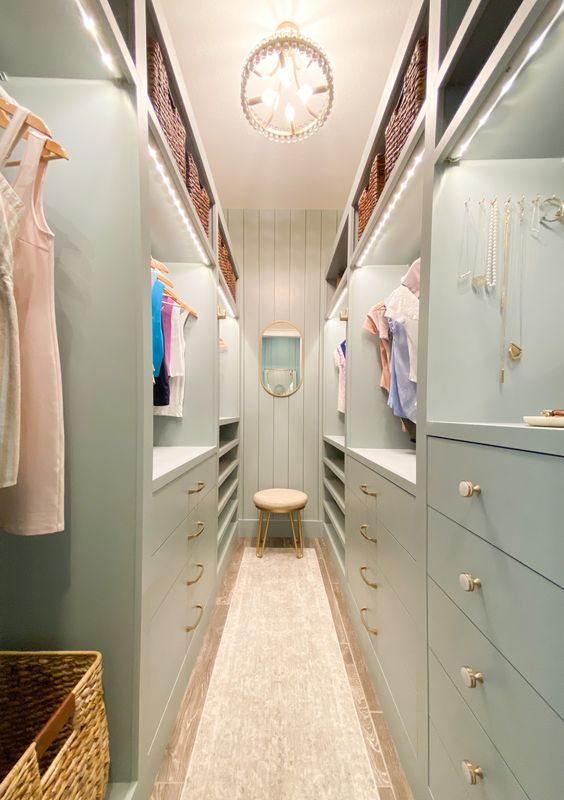 a mint green narrow closet with lots of drawers and open storage compartments, with lit up shelves and a chandelier