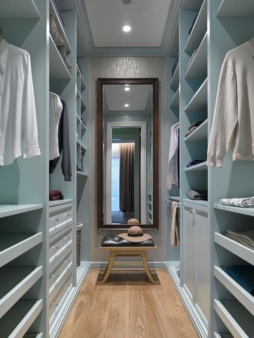 a narrow blue closet with open storage compartments, drawers and railings, a mirror and a black leather stool