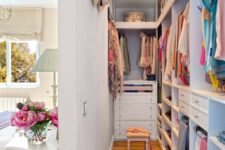 a narrow closet with open storage compartments, drawers, railings and lights, a har organizer hanging on the wall