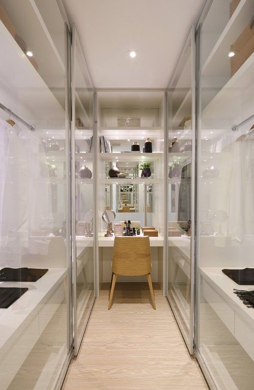 a narrow walk in closet with glass sliding doors that cover all the storage units and a vanity in the end of the space