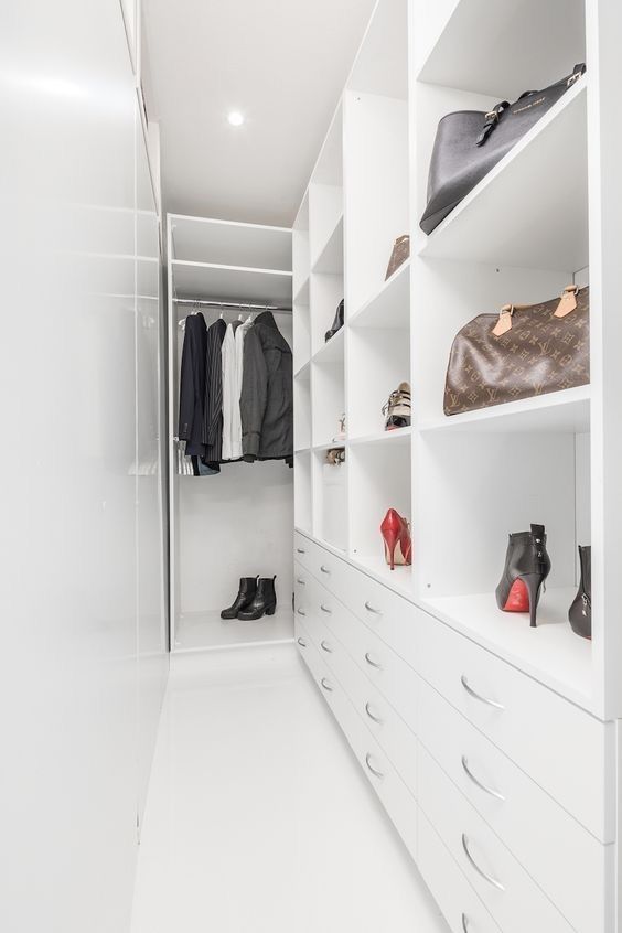 a narrow white walk-in closet with railing, open storage compartments, drawers and some clothes and shoes