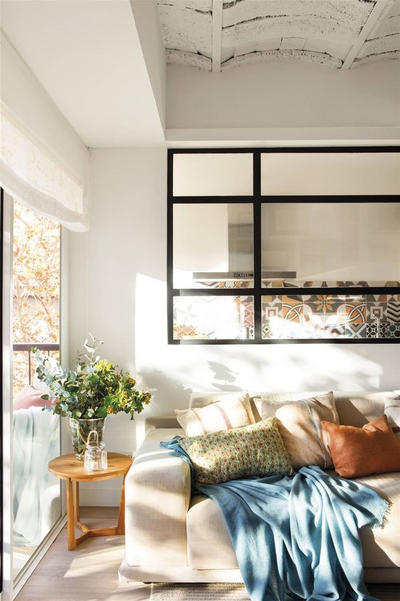 a neutral and muted color living room styled with a large black frame window that leads to the kitchen and lets enjoy natural light