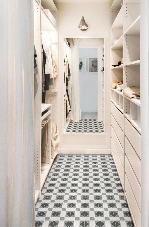 a neutral and warm colored narrow closet with open storage compartments, drawers and shelves plus some railings and a large mirror