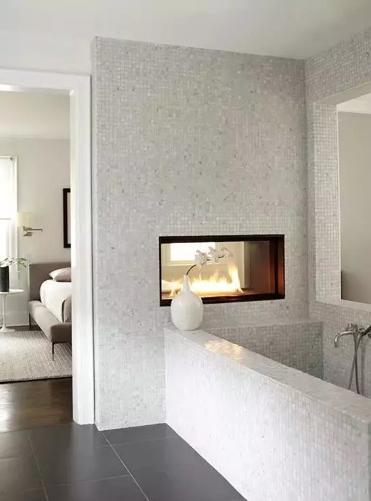 a neutral bathroom with small scale tiles, a double-sided fireplace, a bathtub clad with tiles is a chic idea to rock