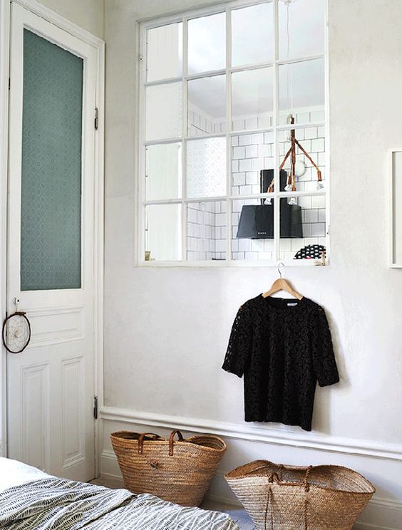 a small Scandi bedroom connected to the kitchen through a large window with white frames lets more light inside both spaces