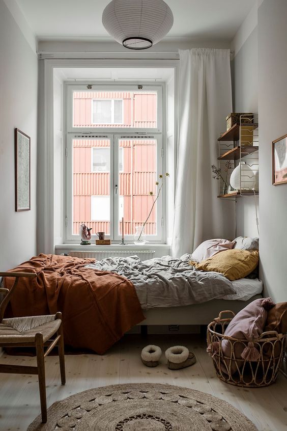 a small Scandinavian bedroom with a casement window and a clerestory addition on top, with a bed with muted color bedding and a wall-mounted shelf