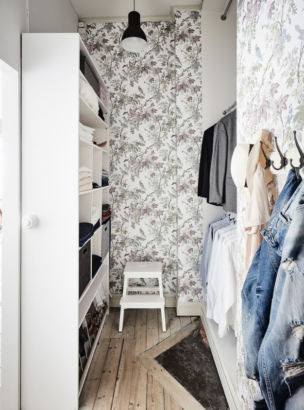 a small and lovely walk-in closet with botanical wallpaper, a white storage unit and railings for hanging clothes and steps