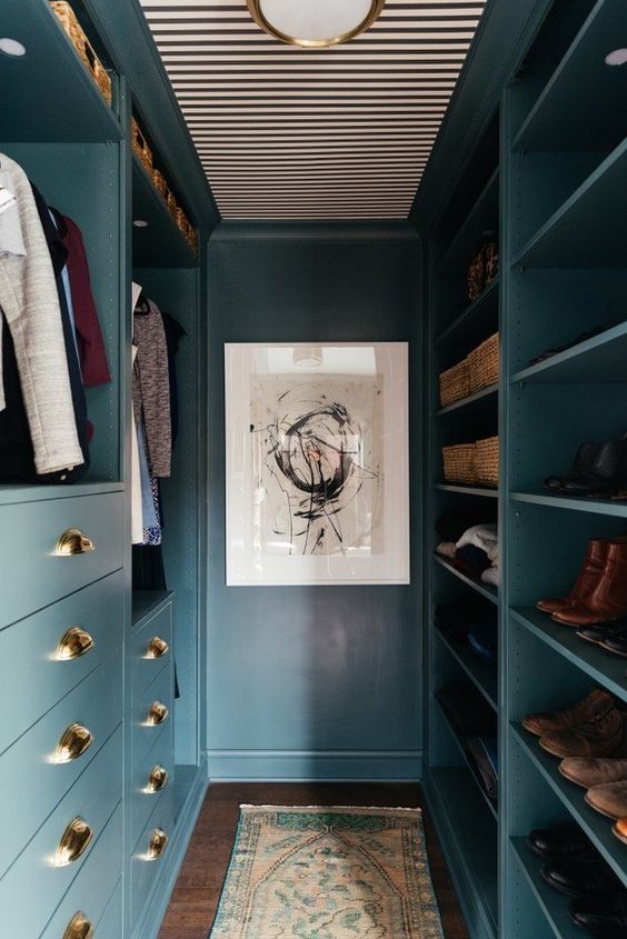 a small and narrow blue closet made of IKEA Pax wardrobes, with open compartments, shelves and drawers, a chandelier and some boxes