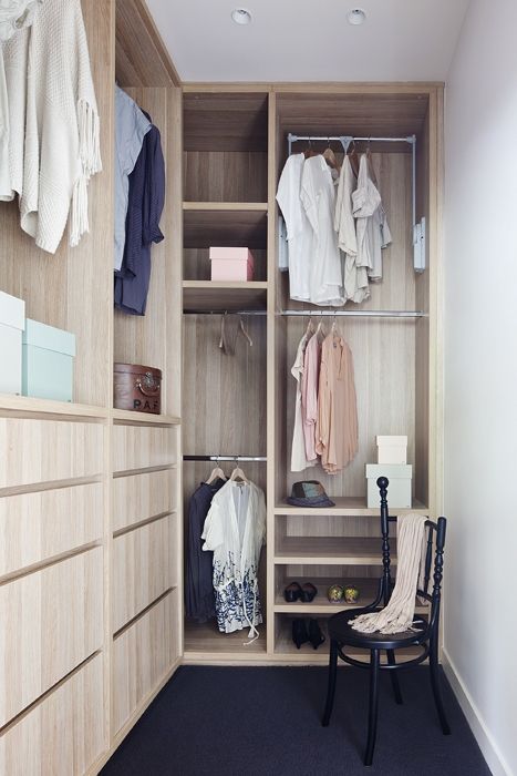 a small and narrow walk in closet with light stained drawers, open storage compartments and railings, a black vintage chair