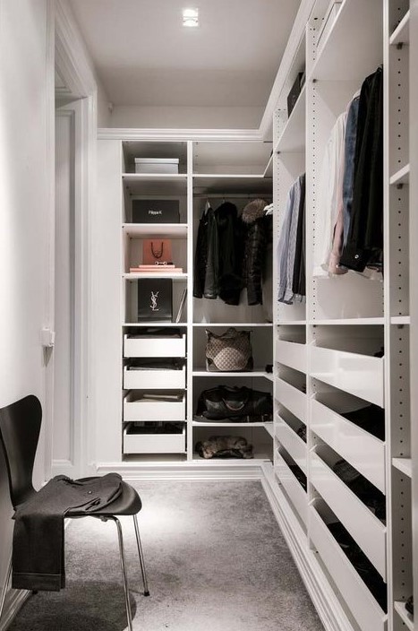 a small minimalist closet with holders for hangers, lots of drawers, open shelves and a single black chair