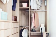 a small stylish closet done in light stained wood, with holders for clothes hangers, some open shelves, built-in drawers and a black chair