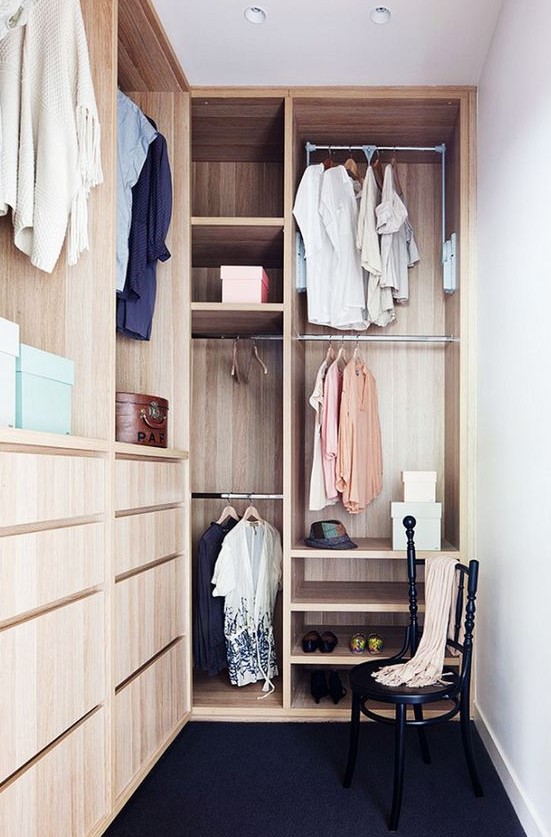 a small stylish closet done in light stained wood, with holders for clothes hangers, some open shelves, built-in drawers and a black chair