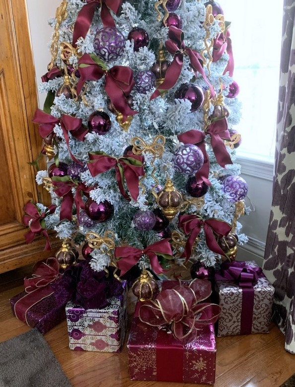 a sophisticated flocked Christmas tree with purple, clear and purple print ornaments, purple and gold ribbon bows