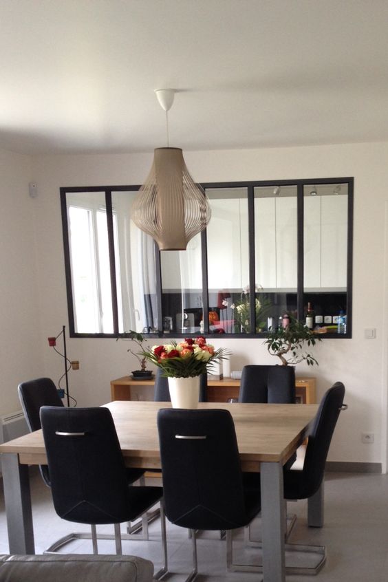 a stylish modern dining space with a large interior window with black frames that connects the space with the kitchen