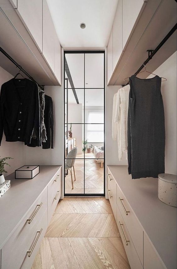 a stylish neutral narrow closet with large open storage compartments, drawers, cabinets on top and some boxes plus a glass door