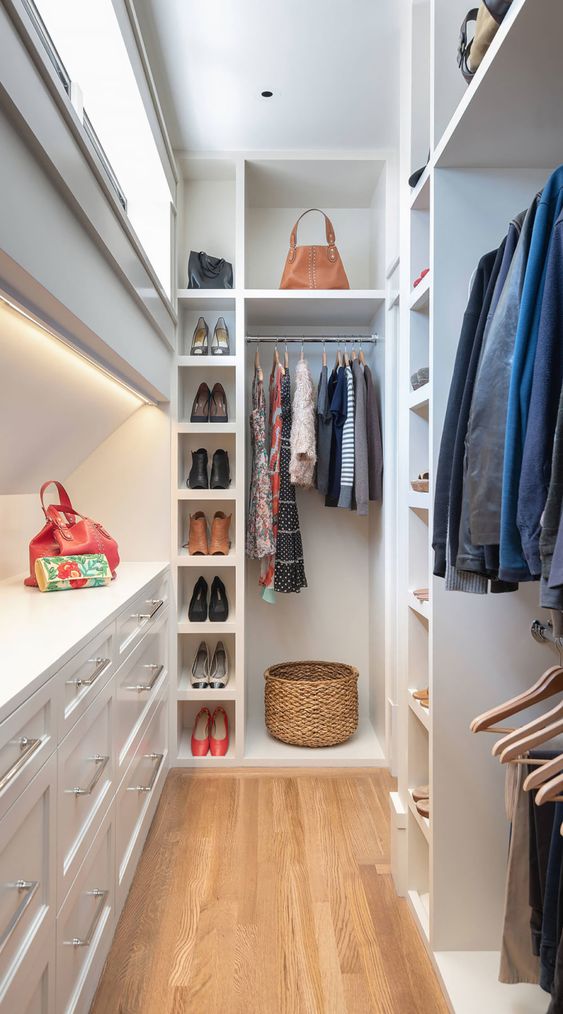 a tall and narrow white closet with lots of shelves, open storage compartments, railings for clothes and built in lights