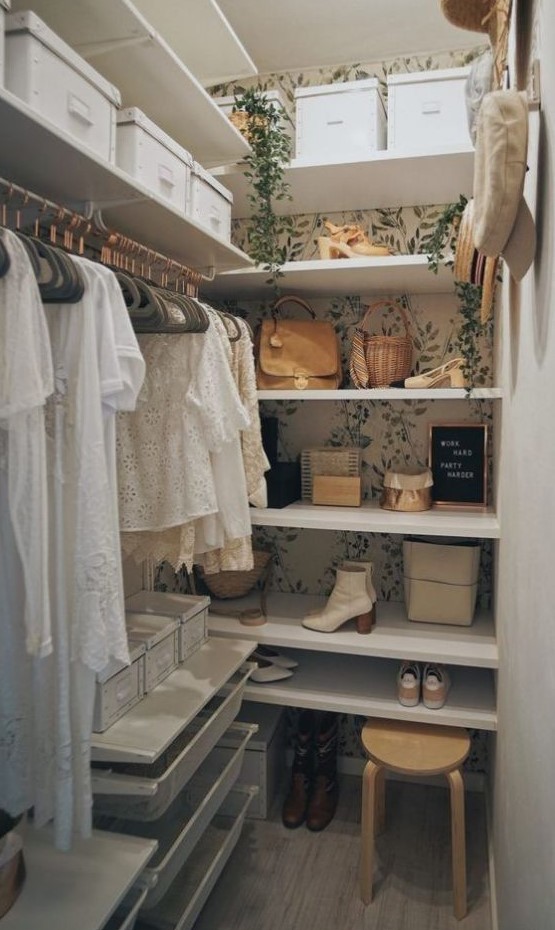 a tiny girlish closet with botanical wallpaper, a faux cascading plant, open shelves, some cubbies, holders for hangers and a wooden stool