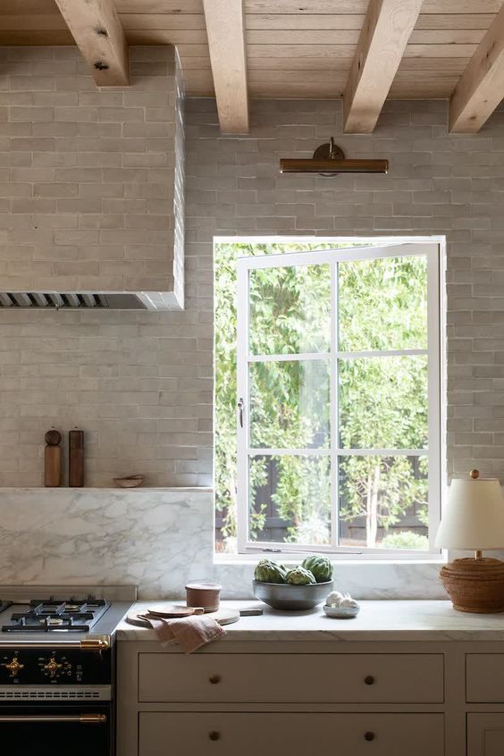 a welcoming neutral kitchen with grey cabinets and tiles, white marble and a casement window with paning