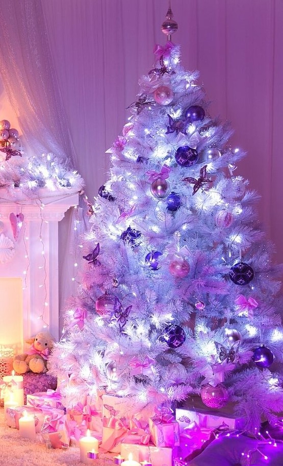 a white Christmas tree with pink and purple ornaments, lights and a tree topper plus candles around is amazing