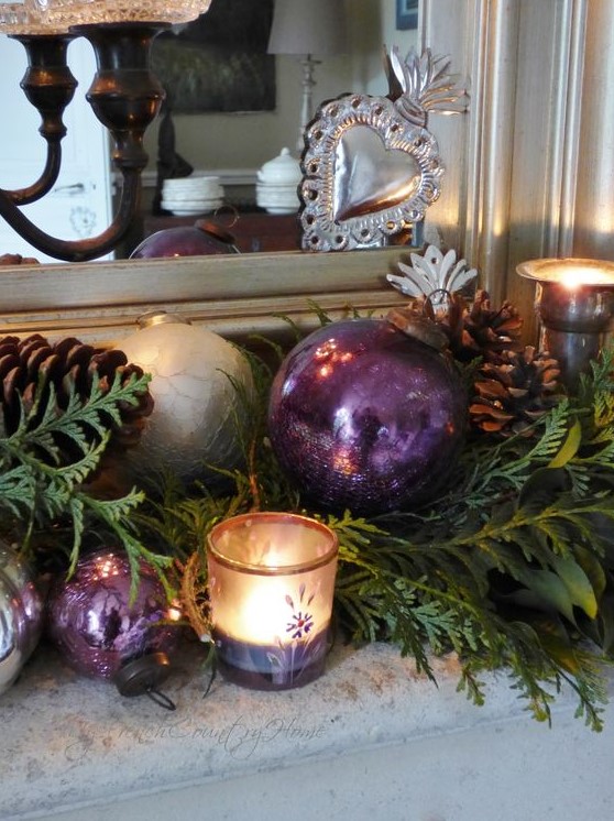 delicate and refined Christmas mantel decor with greenery, pinecones, purple and silver ornaments and candleholders is very chic and cool
